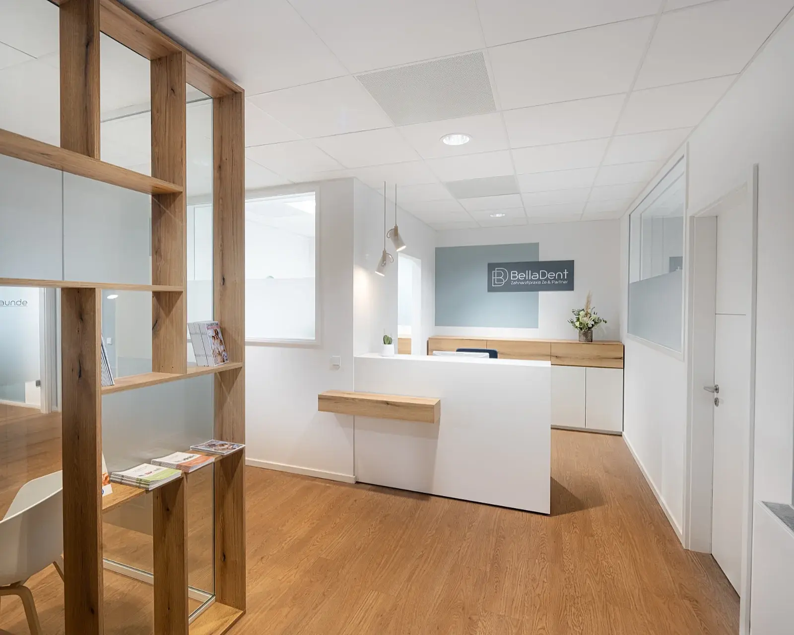 Empfangstresen-Detail von Matthias Knab: Haptischer Kontrast zwischen Holzfurnier und weißen Oberflächen in der Zahnarzt Praxis Bella Dent in Heidelberg; Fokus auf die horizontale Linienführung im Praxis-Design.